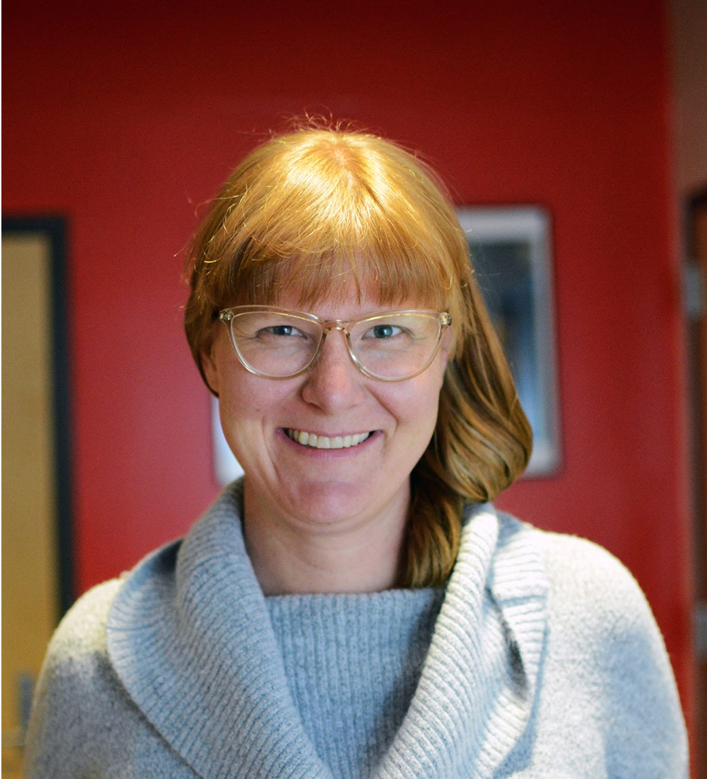 Portrait picture of Abigale Stangl, a woman with long red hair wearing a gray sweater and glasses looking straight at the camera and smiling