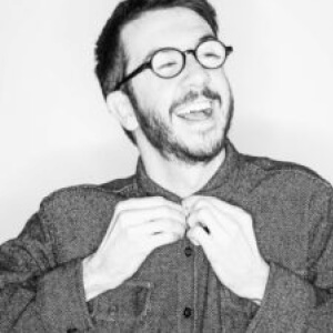 A headshot of Will, a man with short hair and a beard, wearing a button-up shirt and glasses, looking upwards, smiling